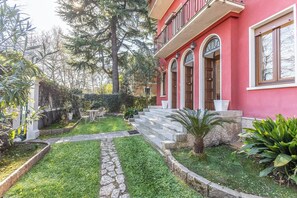 A red building with a stone pathway leading to a set of stairs, surrounded by greenery and trees. - -Stanza con bagno privato 8 - uso cucina -Bastioni (Verona)