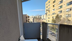 A balcony with a white table and chairs, a small black bowl, and a view of a cityscape with buildings and parked cars. - Appartamento La Sosta (Verona)