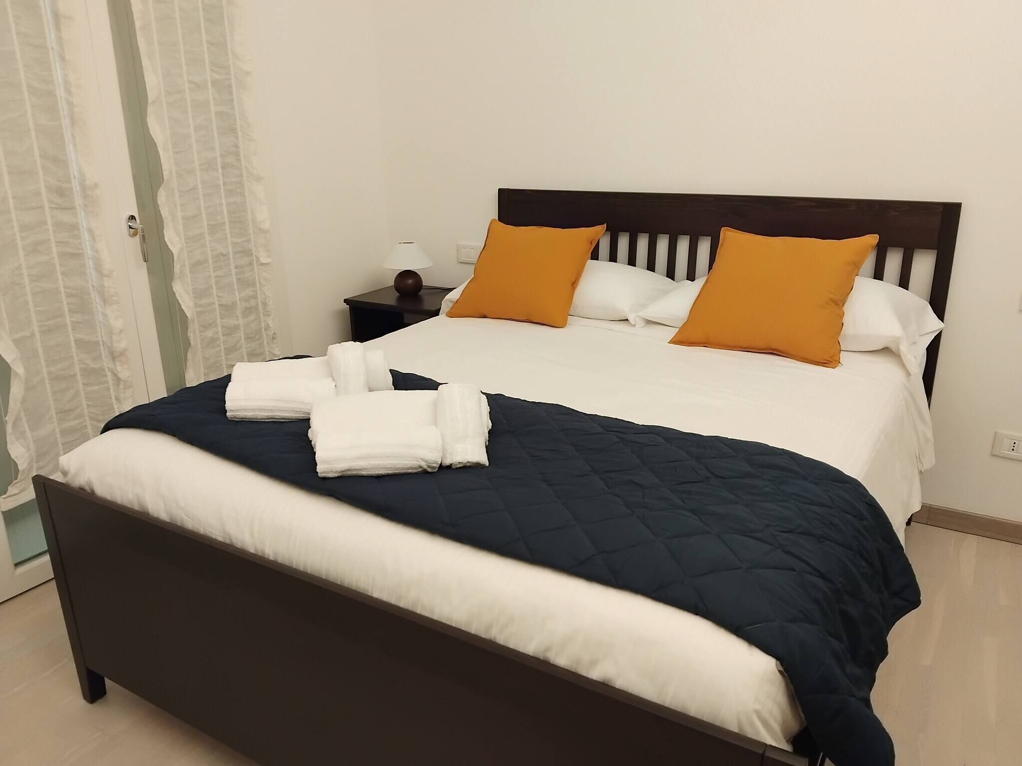 A neatly made bed with a dark headboard, white and blue bedding, and two orange pillows.