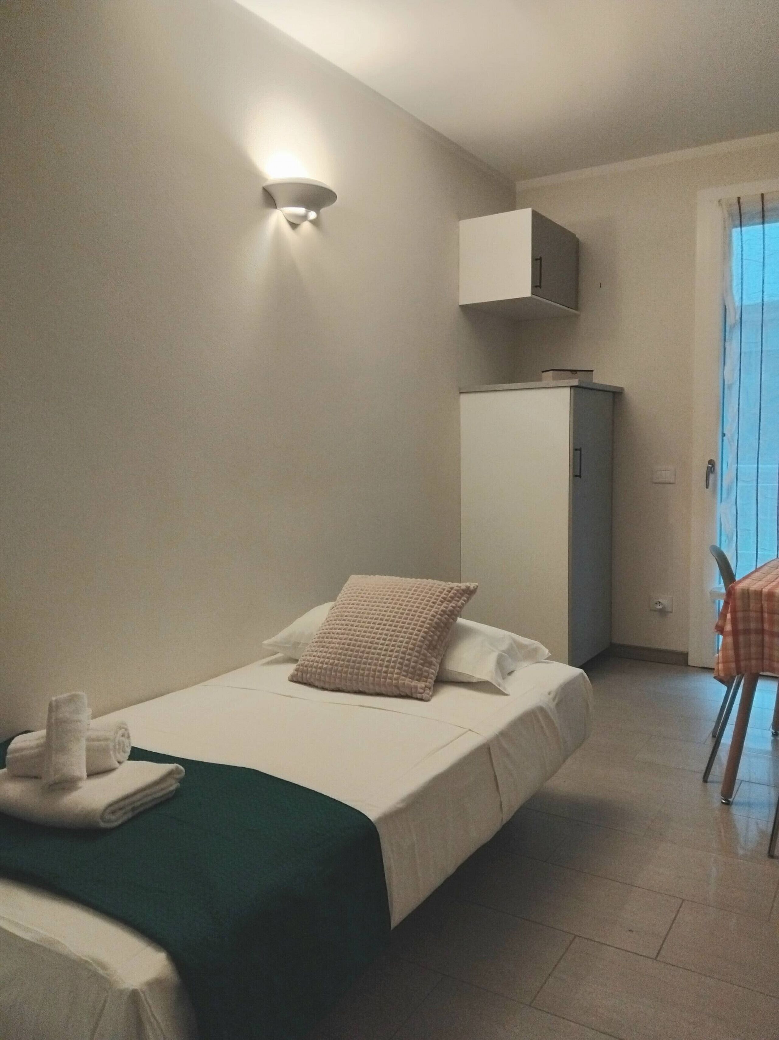 Ein Hotelzimmer mit Bett, einem kleinen Tisch, einem Schrank und einer Wandleuchte.