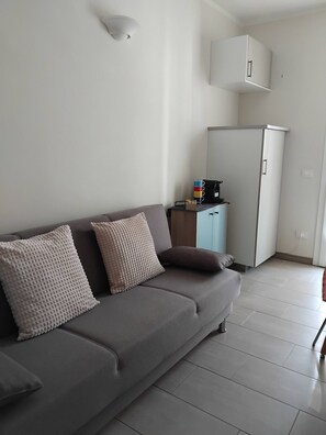 A modern living room with a grey sofa, two patterned cushions, a white cabinet, and a small table with a kettle. - Appartamento La Sosta (Verona)