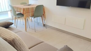A living room with a sofa, a dining table with chairs, and a mounted TV displaying 'NETT'. - Appartamento La Sosta (Verona)