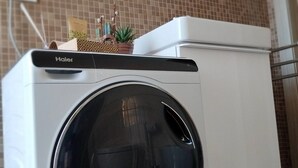 A front-loading Haier washing machine with a control panel on top, placed on a kitchen counter with a tiled backsplash. - Appartamento La Sosta (Verona)