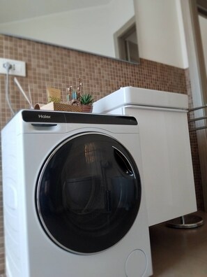 Eine Haier Waschmaschine mit Frontlader und Bedienfeld oben, auf einer Küchenarbeitsplatte mit Fliesenrückwand platziert.