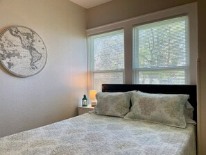 A bedroom with a bed, two windows with blinds, a nightstand with a lamp, and a wall-mounted globe. - “Bayview Shores" Stylish Lakefront Ground Level! (Toledo)