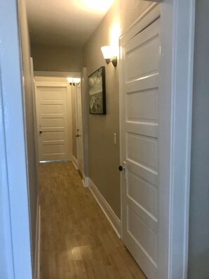 A hallway with wooden flooring, white doors, and wall-mounted light fixtures.