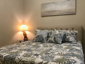 A bed with a floral bedspread, a nightstand with a lamp, and a painting on the wall.