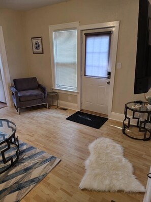 A living room with a sofa, a round coffee table, a fluffy rug, and a door with a window.