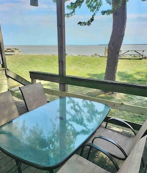 An outdoor patio with a glass-top table and chairs, overlooking a body of water.