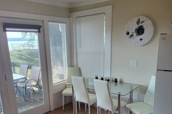 A room with a glass table and white chairs, a door leading outside, and a wall-mounted decorative plate.