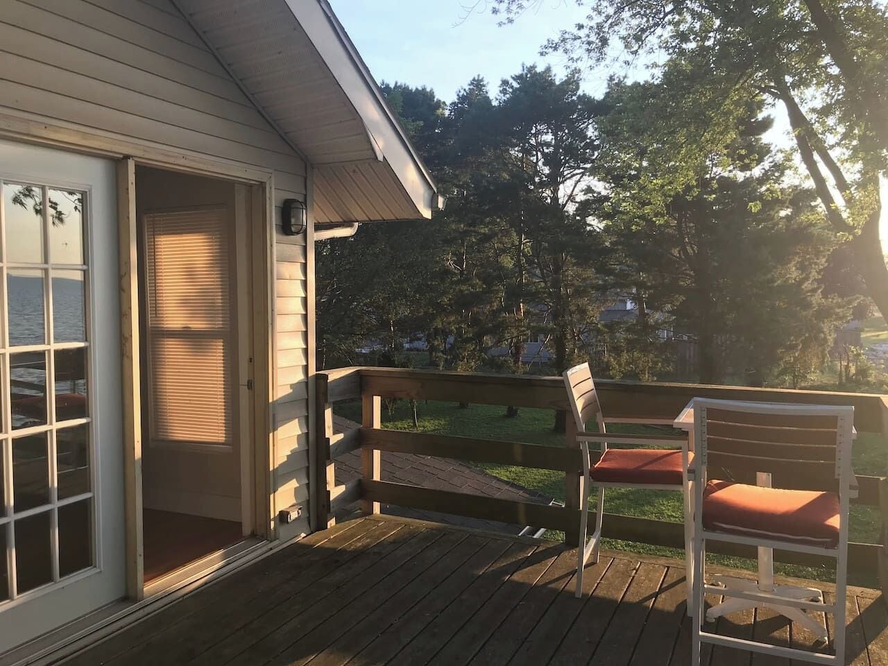 A wooden deck with a bench and a door leading to a covered porch.