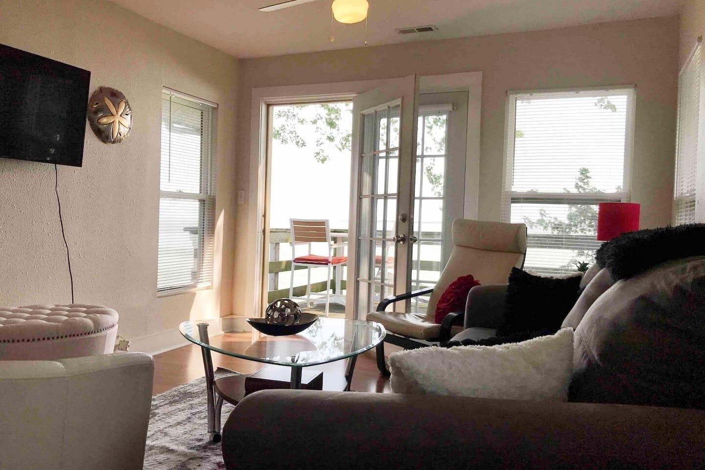 Un salon avec une table basse en verre, un canapé blanc, un fauteuil et un téléviseur fixé au mur.