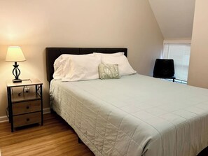 A bedroom with a bed, a nightstand, a lamp, and a window with blinds.