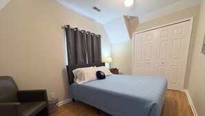 A bedroom with a bed, a chair, a nightstand, a lamp, and a closet.