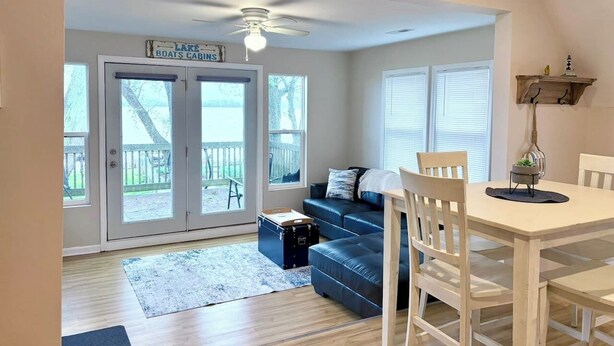 A room with a dining table, chairs, a sofa, a ceiling fan, and a view of a deck through glass doors.