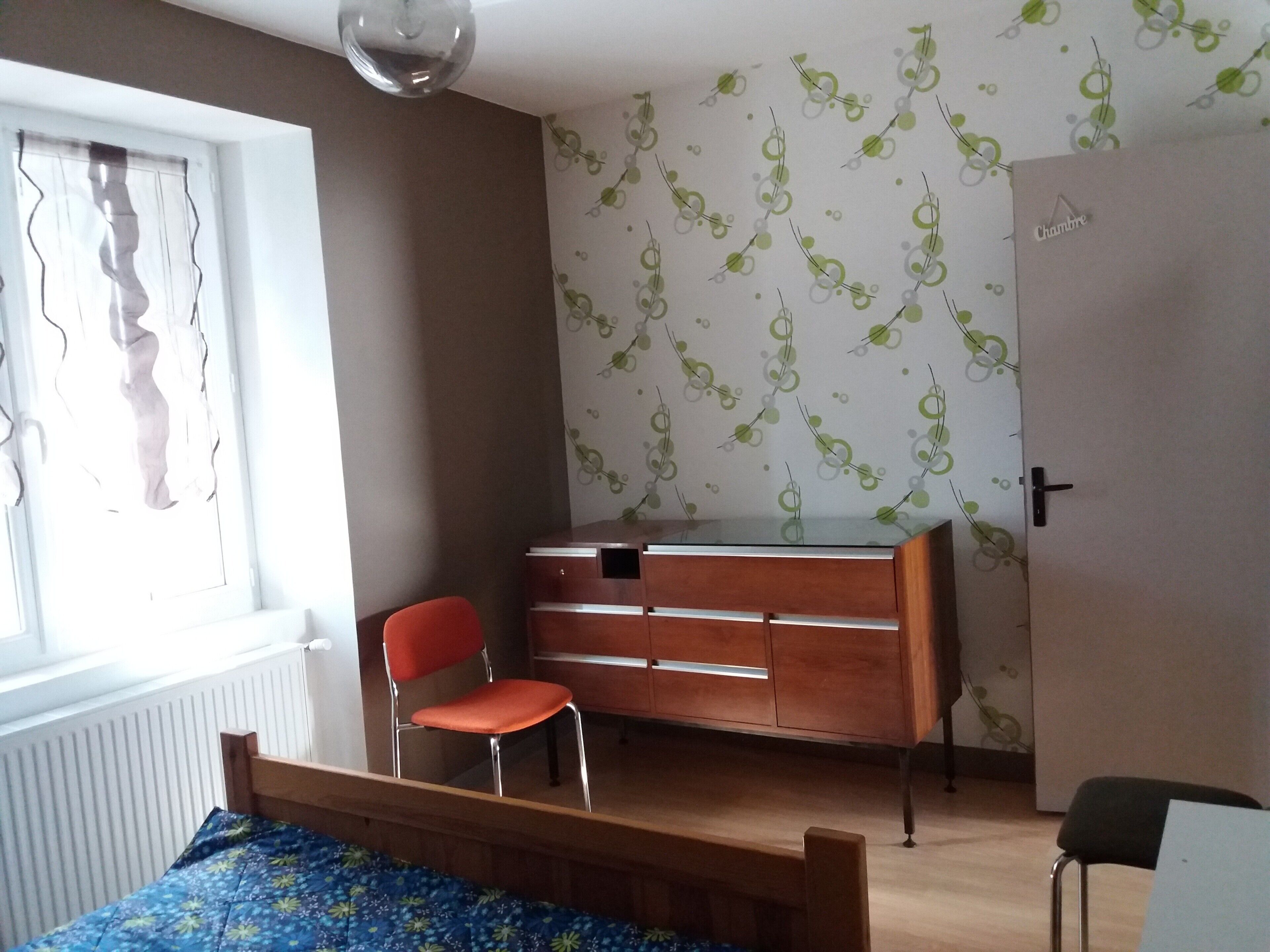 A bedroom with a bed, a dresser, a chair, and a radiator.
