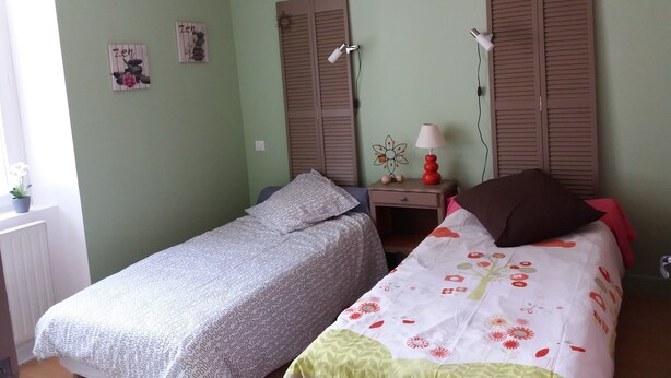 Een slaapkamer met twee bedden, een nachtkastje, een lamp en een raam met jaloezieën.