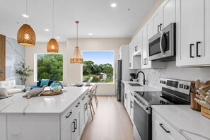 A modern kitchen with white cabinetry, stainless steel appliances, and a large island with seating. - 3002 Blue Lagoon C | Luxe Group Getaway, Steps to Beach, Lagoon Views (Panama City Beach)