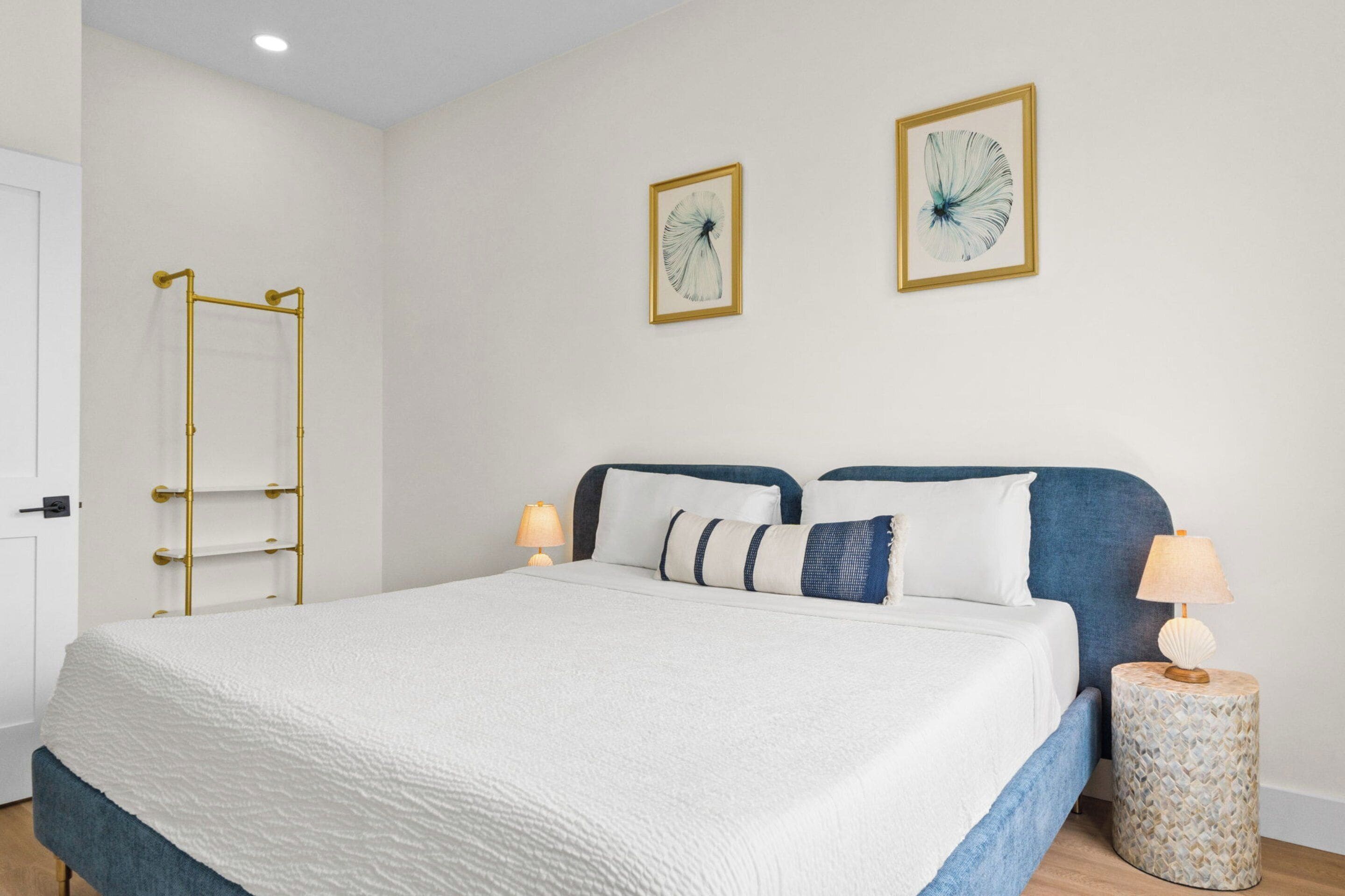 Un dormitorio con una cama, lámparas de noche, una escalera fijada a la pared y dos cuadros enmarcados.