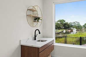 A bathroom with a white marble sink, a black faucet, and a wooden cabinet. There is a round mirror with a gold frame on the wall. - 3002 Blue Lagoon C | Luxe Group Getaway, Steps to Beach, Lagoon Views (Panama City Beach)