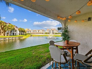 A patio with a table and chairs overlooking a water body and buildings. - Edgewater Villa #2103 | Updated Villa, Lush Views, Resort Amenities (Panama City Beach)