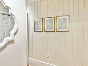 Ein Korridor mit einer weißen Tür und drei gerahmten Kunstwerken an der Wand.