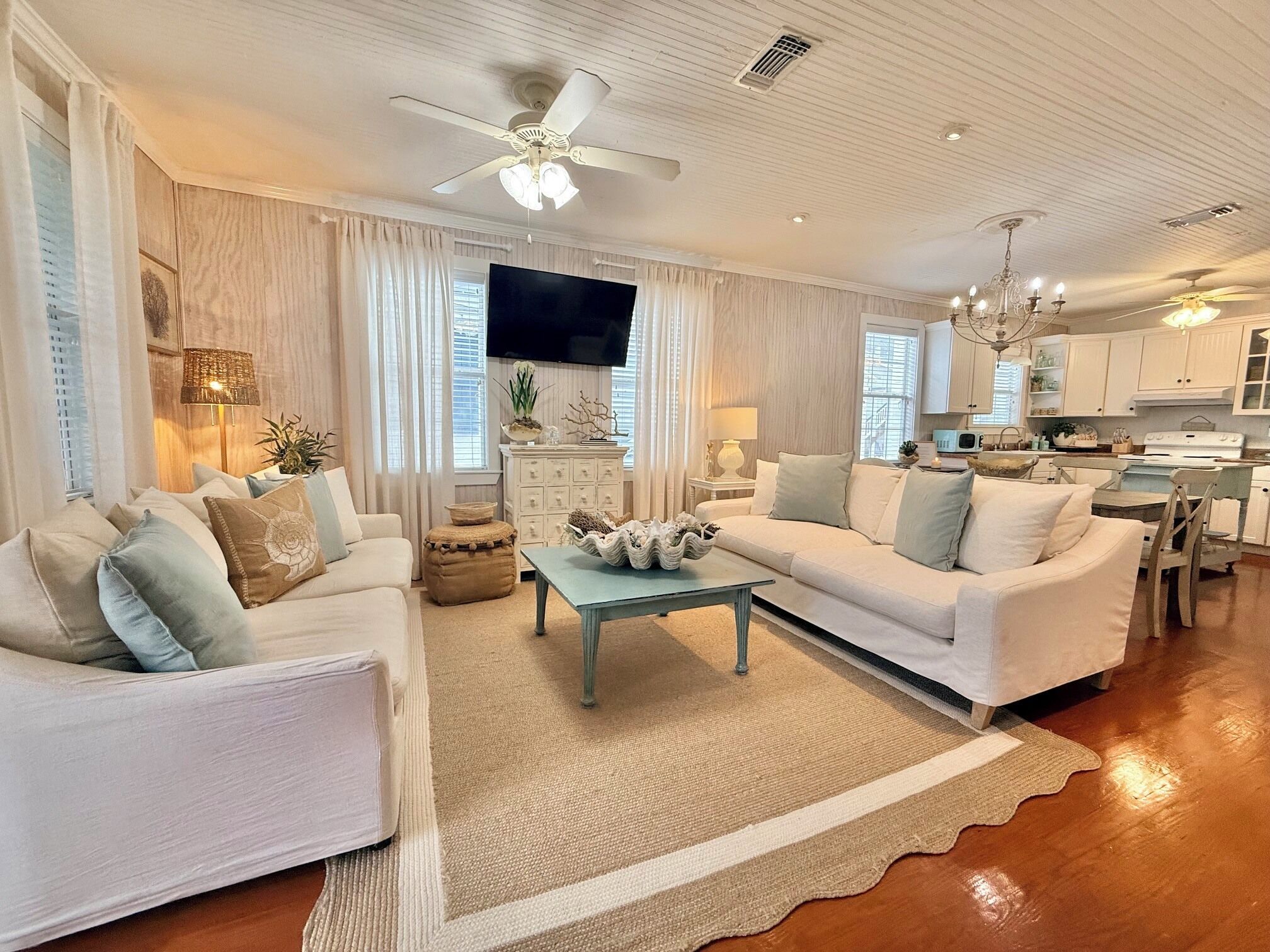 A spacious living room with a white sofa set, a coffee table, and a television.