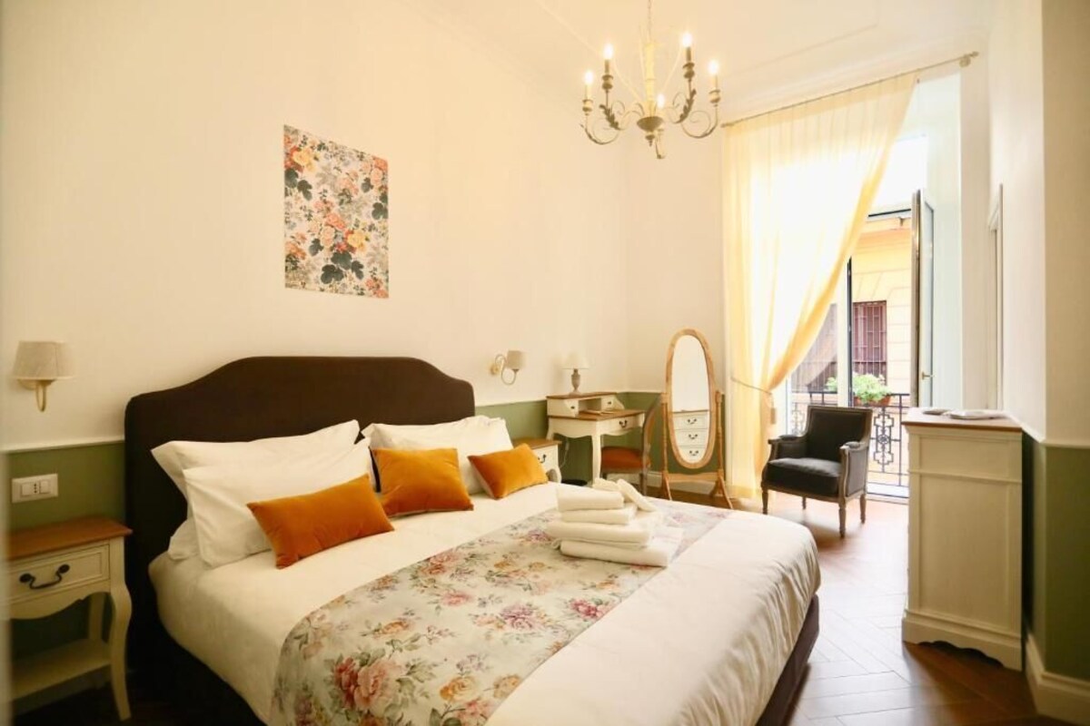 Quarto de hotel com cama, mesa de cabeceira, espelho, cadeira e vista para o exterior.