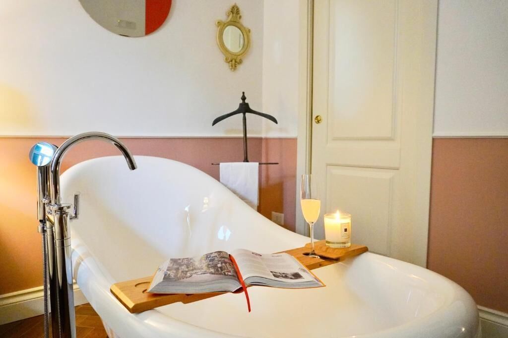 A bathroom with a white bathtub, a towel rack, a mirror, and a candle on a tray.