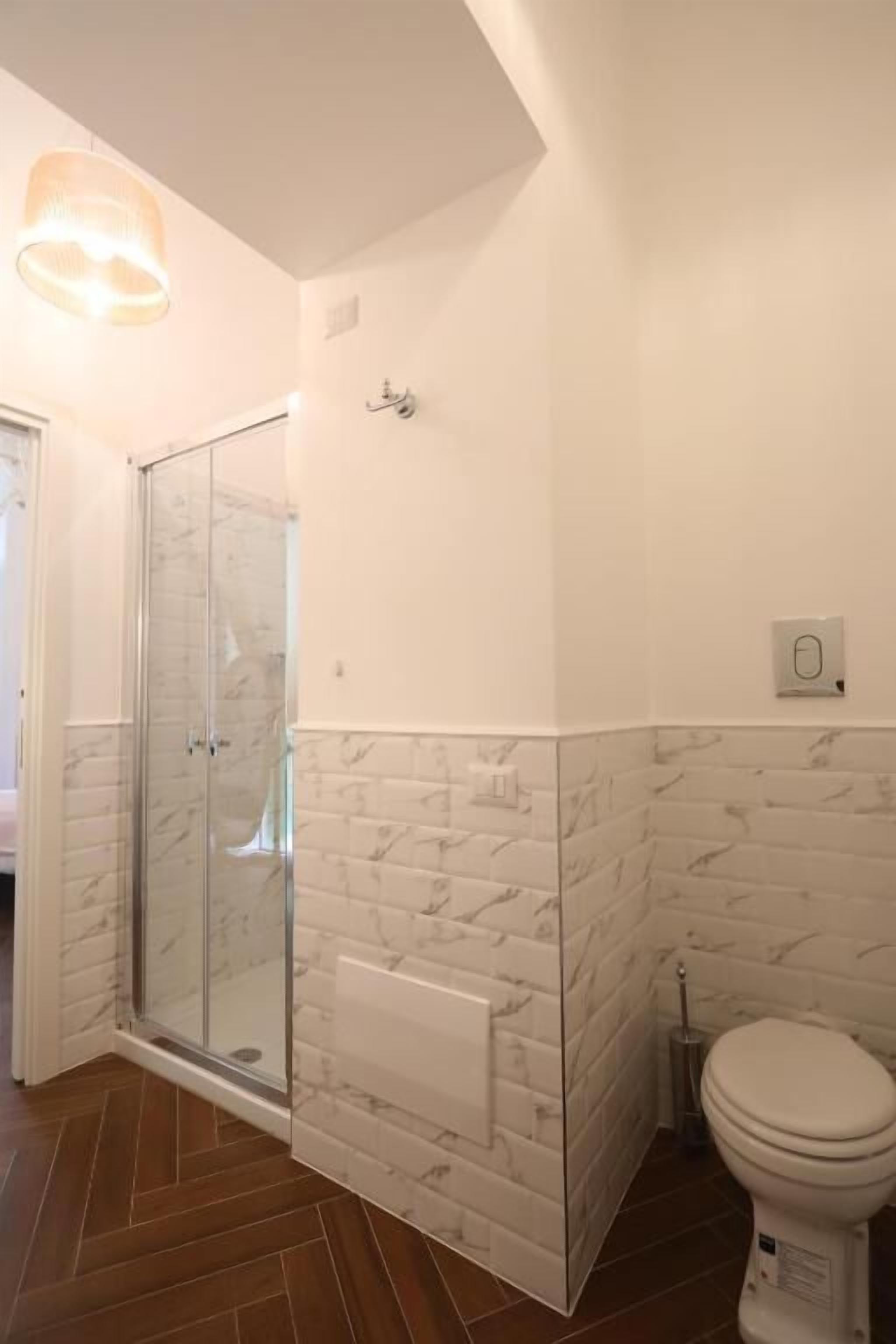 Ein Badezimmer mit Duschkabine aus Glas, Toilette und weiß geflieste Wand mit Marmormuster.