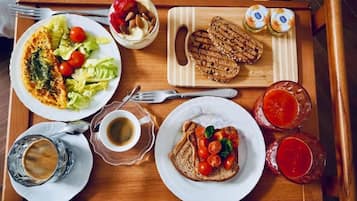 Un vassoio di legno con diversi articoli per la colazione, tra cui pane tostato, un'insalata, un omelette arrotolato e due bicchieri di bevanda rossa.