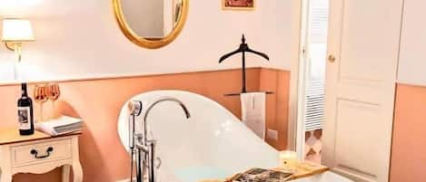 Un baño con una bañera independiente, un tocador con espejo y una puerta que da a otra habitación.
