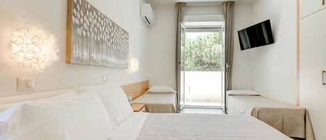 Habitación de hotel con una cama grande, una cama más pequeña, un televisor de pantalla plana y una ventana con cortinas.
