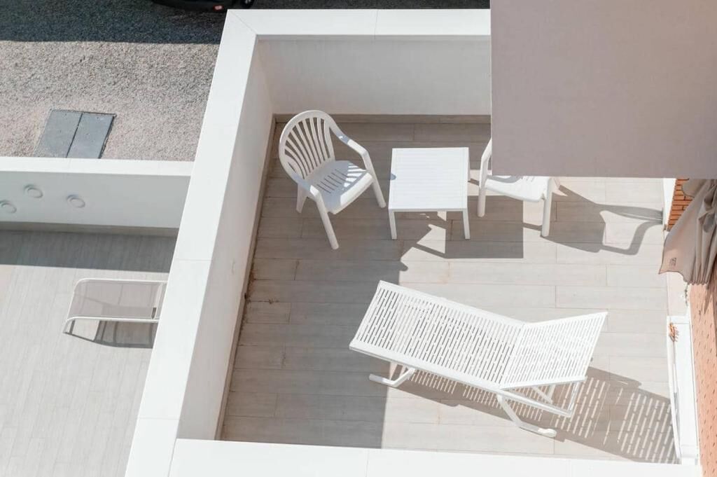 A rooftop terrace with a white chair, a small table, and a white lounge chair.