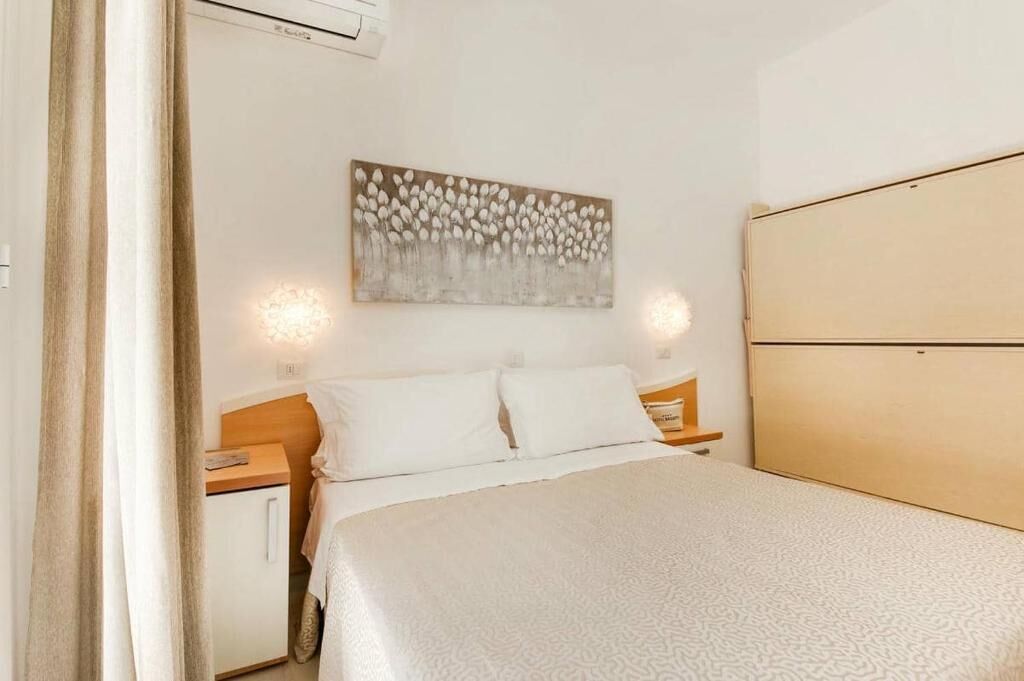 A bedroom with a bed, a nightstand, a bedside table, a wall-mounted artwork, and a wardrobe.