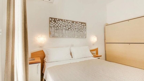 A bedroom with a bed, a nightstand, a bedside table, a wall-mounted artwork, and a wardrobe. - Hotel Bassetti (Cervia)