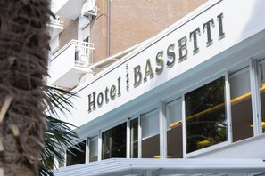 Un hotel con un letrero que dice 'Hotel Bassetti'. Presenta una fachada blanca con varias ventanas y un balcón.