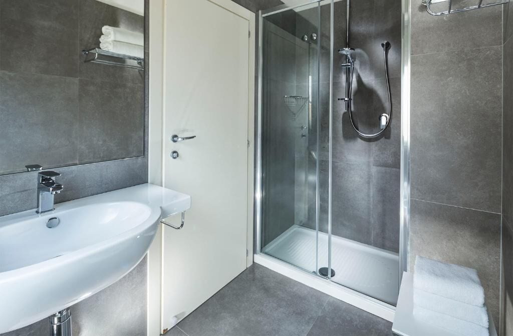 Un baño moderno con un lavamanos blanco, cabina de ducha con vidrio y un perchero.