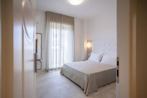 Habitación de hotel con cama, mesita de noche, lámpara de pared y ventana con cortinas.