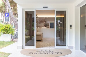 A hotel entrance with a reception desk, a sofa, and a doormat with the hotel's name. - Hotel Bassetti (Cervia)