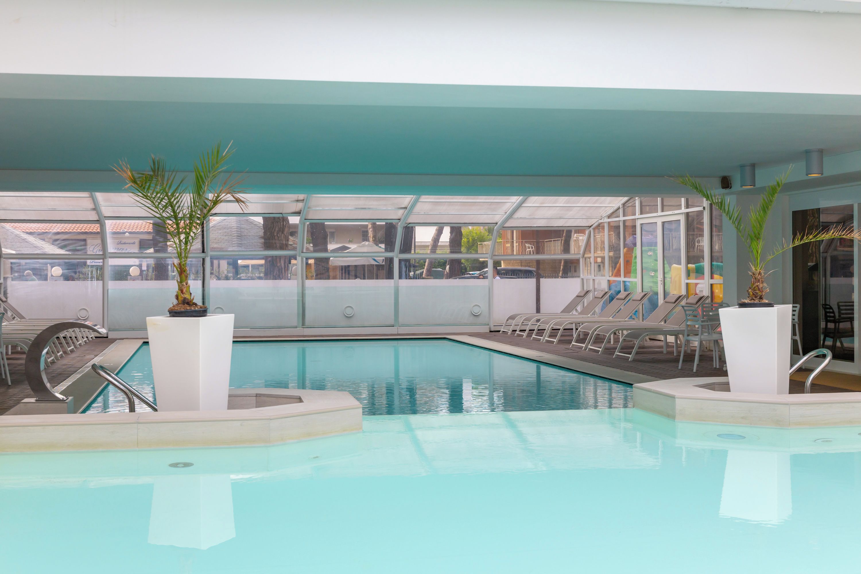An indoor swimming pool with clear water, surrounded by lounge chairs and potted plants.