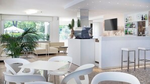 A modern bar area with a flat-screen TV, white bar stools, and a wine rack. - Hotel Bassetti (Cervia)