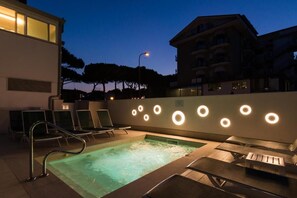 Un área de piscina en la azotea con sillones de descanso, una piscina pequeña y una pared con lámparas circulares.