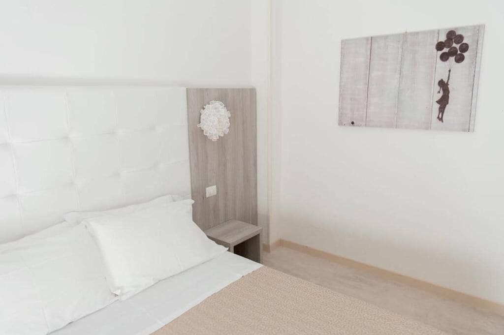 Un dormitorio con cama, mesita de noche, lámpara de pared y un cuadro.