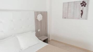 Un dormitorio con cama, mesita de noche, lámpara de pared y un cuadro.