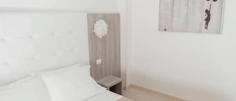 Quarto com cama, mesa de cabeceira, luminária na parede e um quadro.