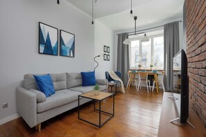 A modern living room with a grey sofa, a coffee table, and a dining area with a table and chairs. - Cosy Apartment with a Desk | Close to the Underground | Smart TV (Warszawa)