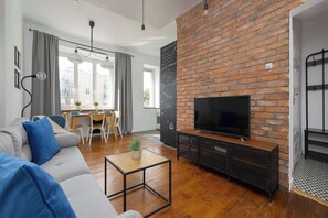 Un salon moderne avec un mur en briques, un téléviseur à écran plat, un canapé et un coin repas comprenant une table et des chaises.