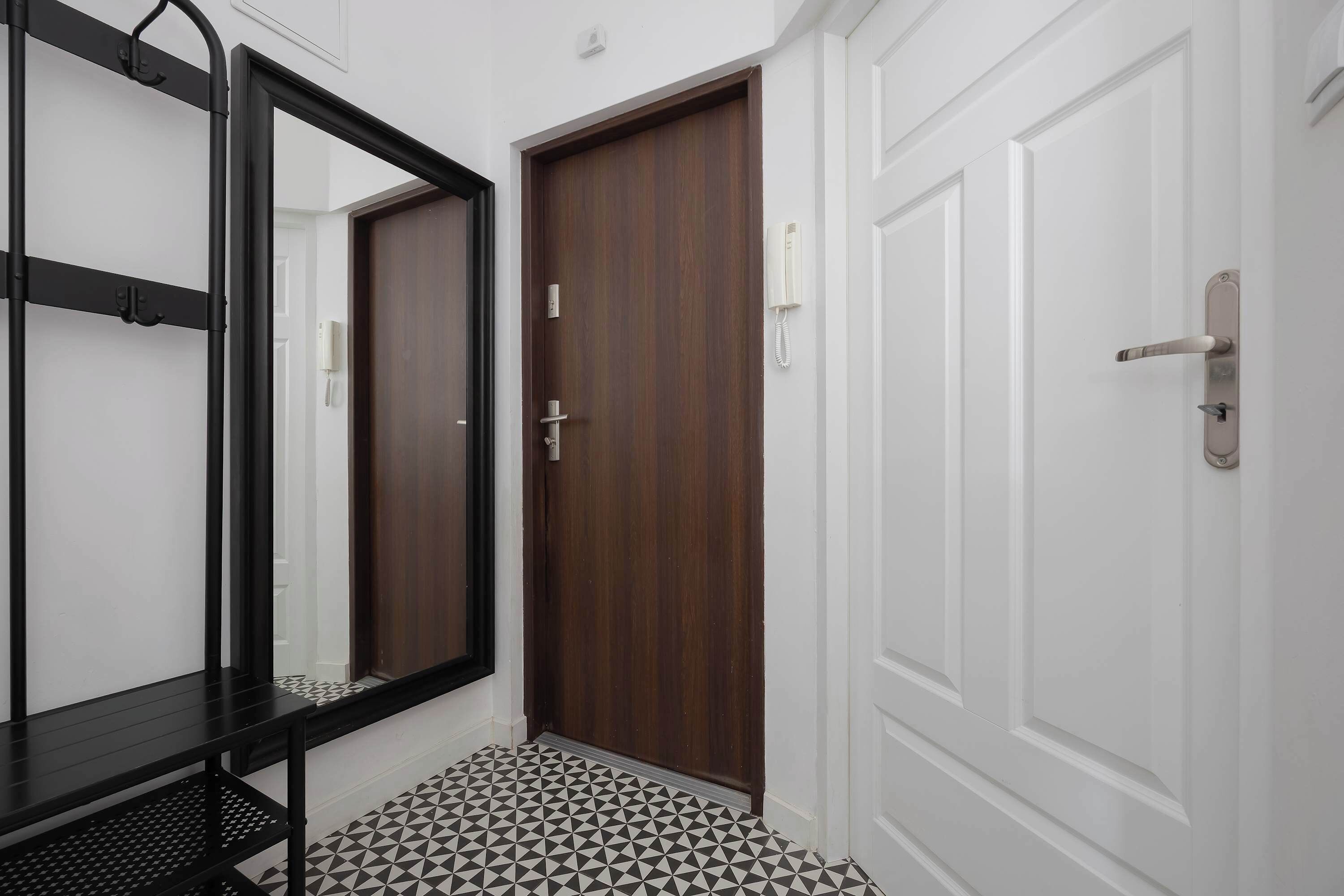 A hallway with a wooden door, a white door, and a black metal bench.