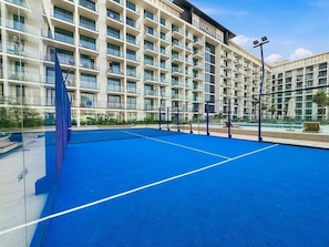 Ein Hotel mit Tennisplatz, mehreren Balkonen und blauem Himmel.
